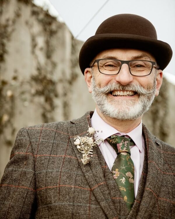 Beaming groom in tweed three-piece suit and bowler hat with dried flower buttonhole, Cornwall wedding portrait