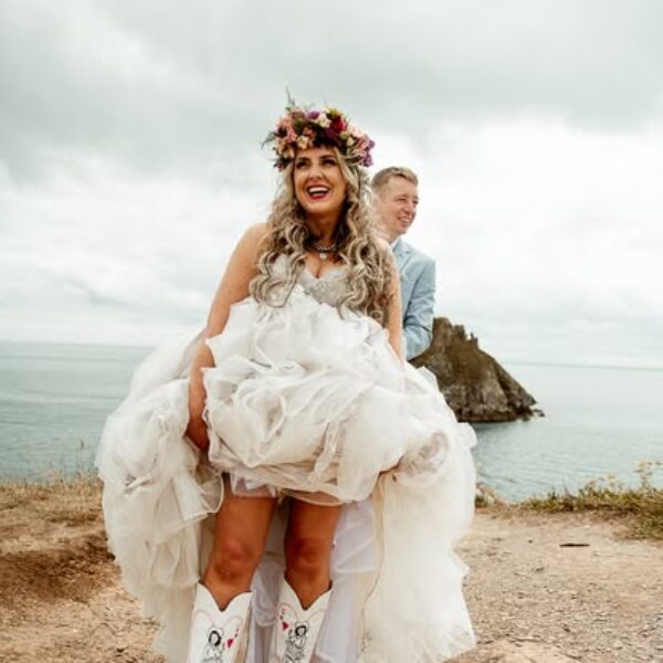 Laughing bride in flower crown with custom cowboy boots at Torbay Devon clifftop wedding