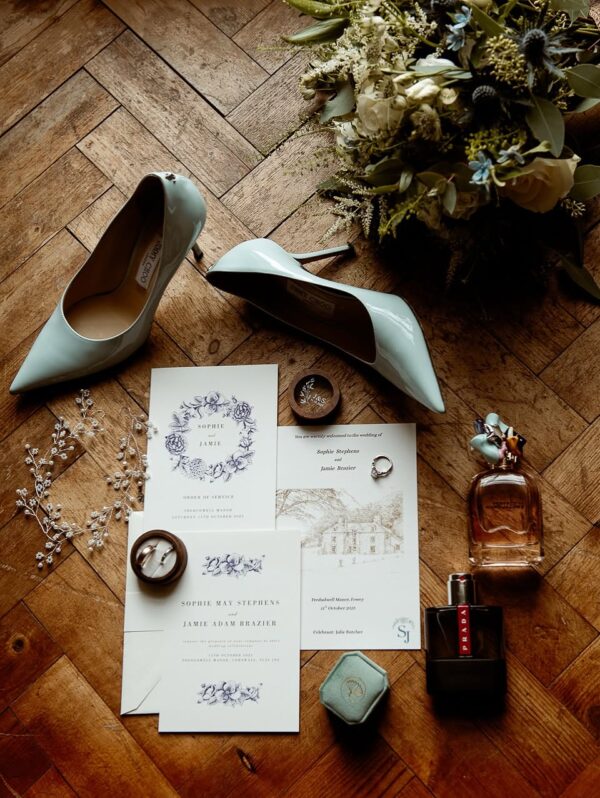 Elegant wedding flat lay showing invitation suite, Jimmy Choo heels, rings and bouquet at Tredudwell Manor Cornwall