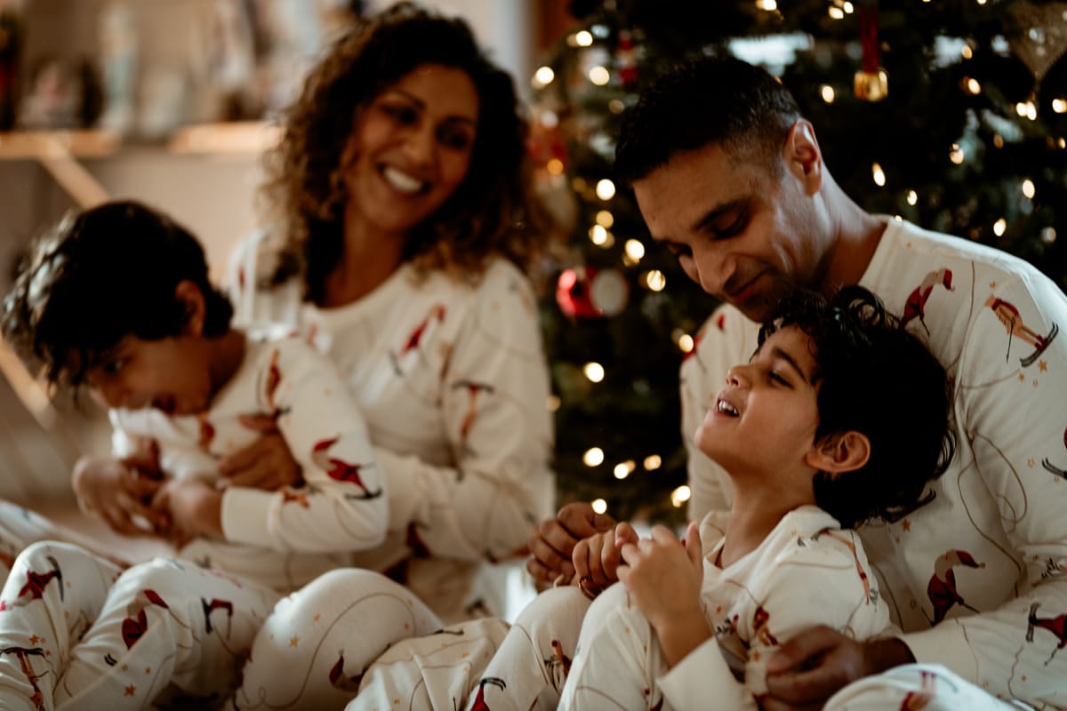 Family of four in matching Christmas pyjamas cuddled together laughing, Cornwall family photoshoot