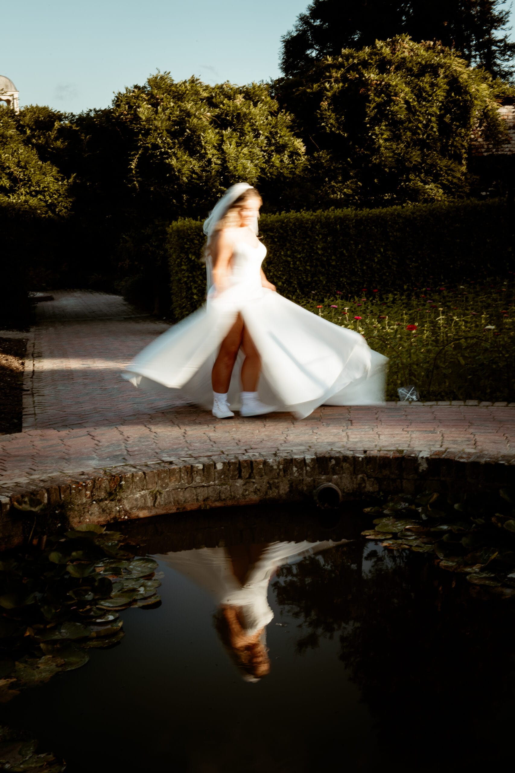 Bride twirling in white gown beside garden pond at Lost Gardens of Heligan Cornwall