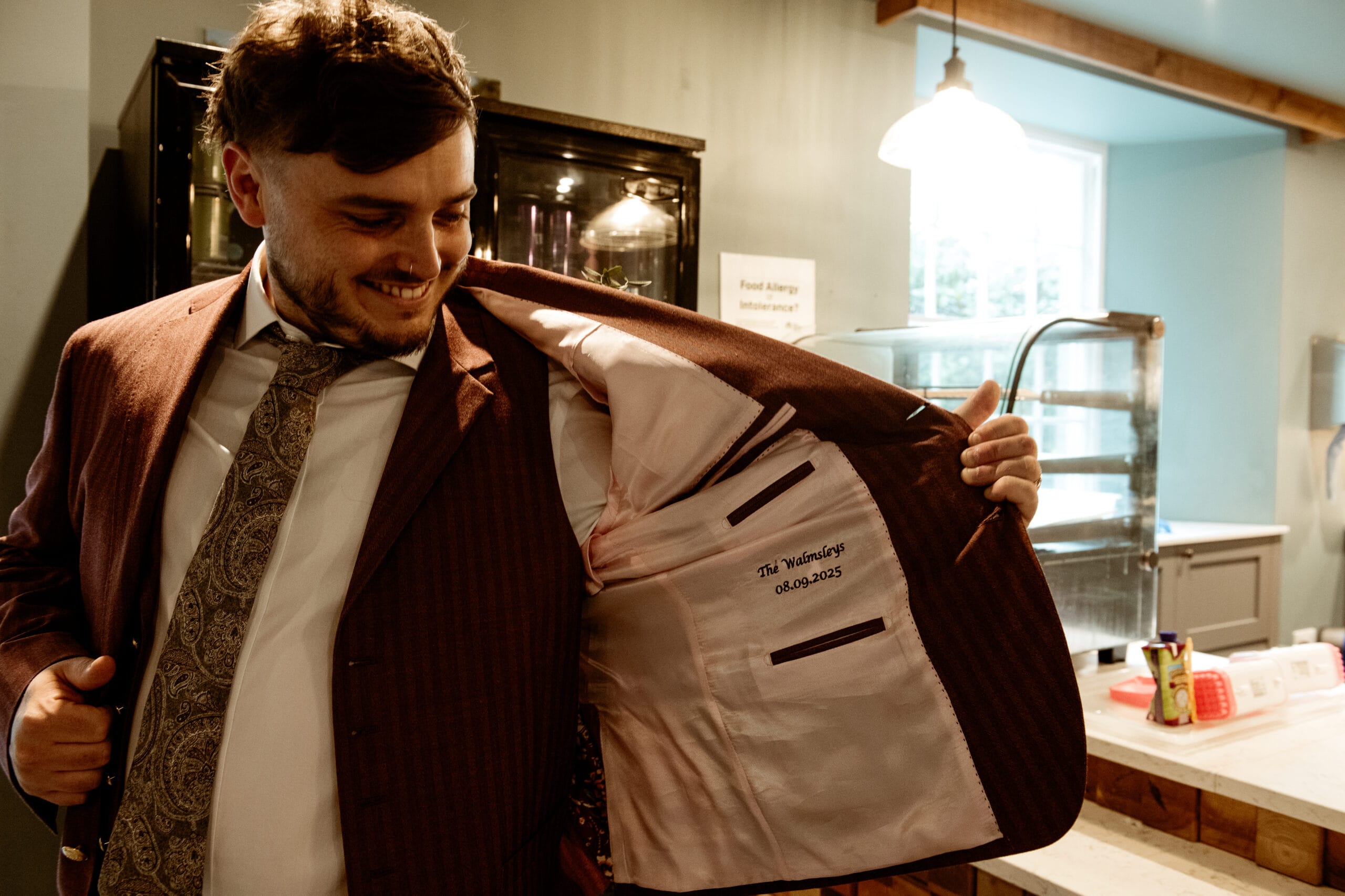 Groom smiling and adjusting burgundy jacket during Cornwall wedding at Lost Gardens of Heligan
